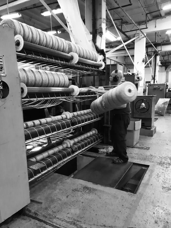 services-01 Black and white image of a man working in a textile factory operating machinery.
