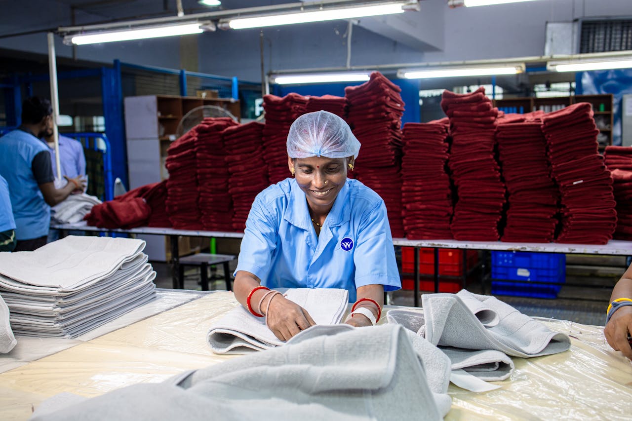 services-02 A woman working in a textile factory, folding fabric with stacks of cloth in background.