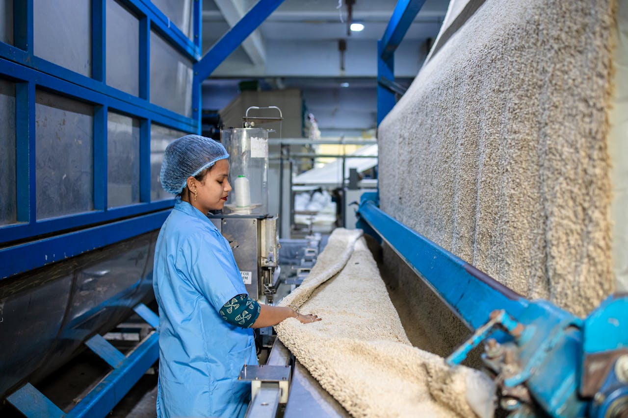 our-story A woman in blue uniform operates machinery in a textile factory, showcasing industrial work.