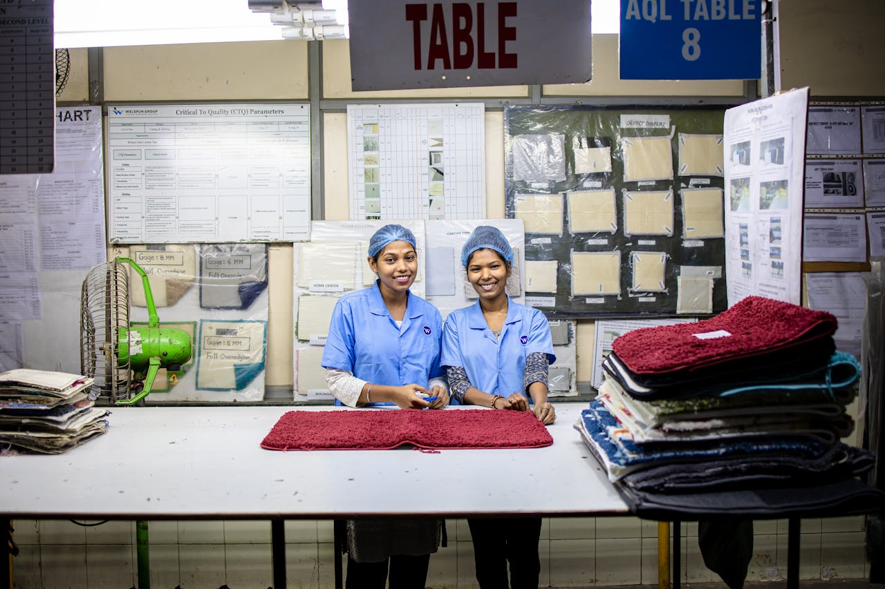 services-04 Two women working in a textile factory, folding fabrics with smiles.