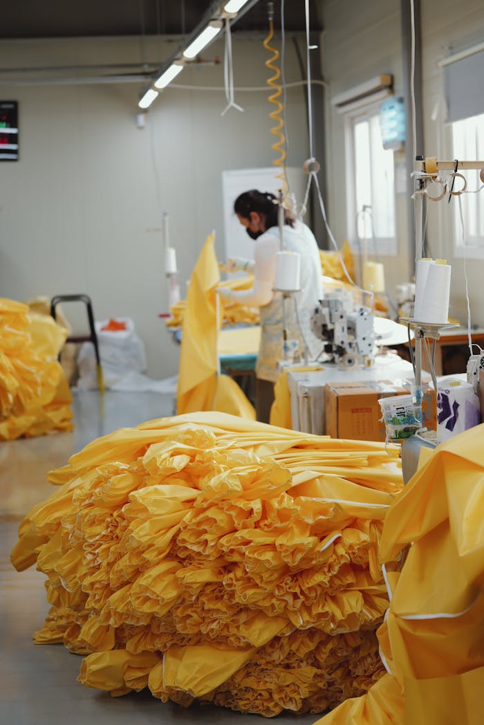 about-us Textile worker manages bright yellow fabric at sewing station in factory.