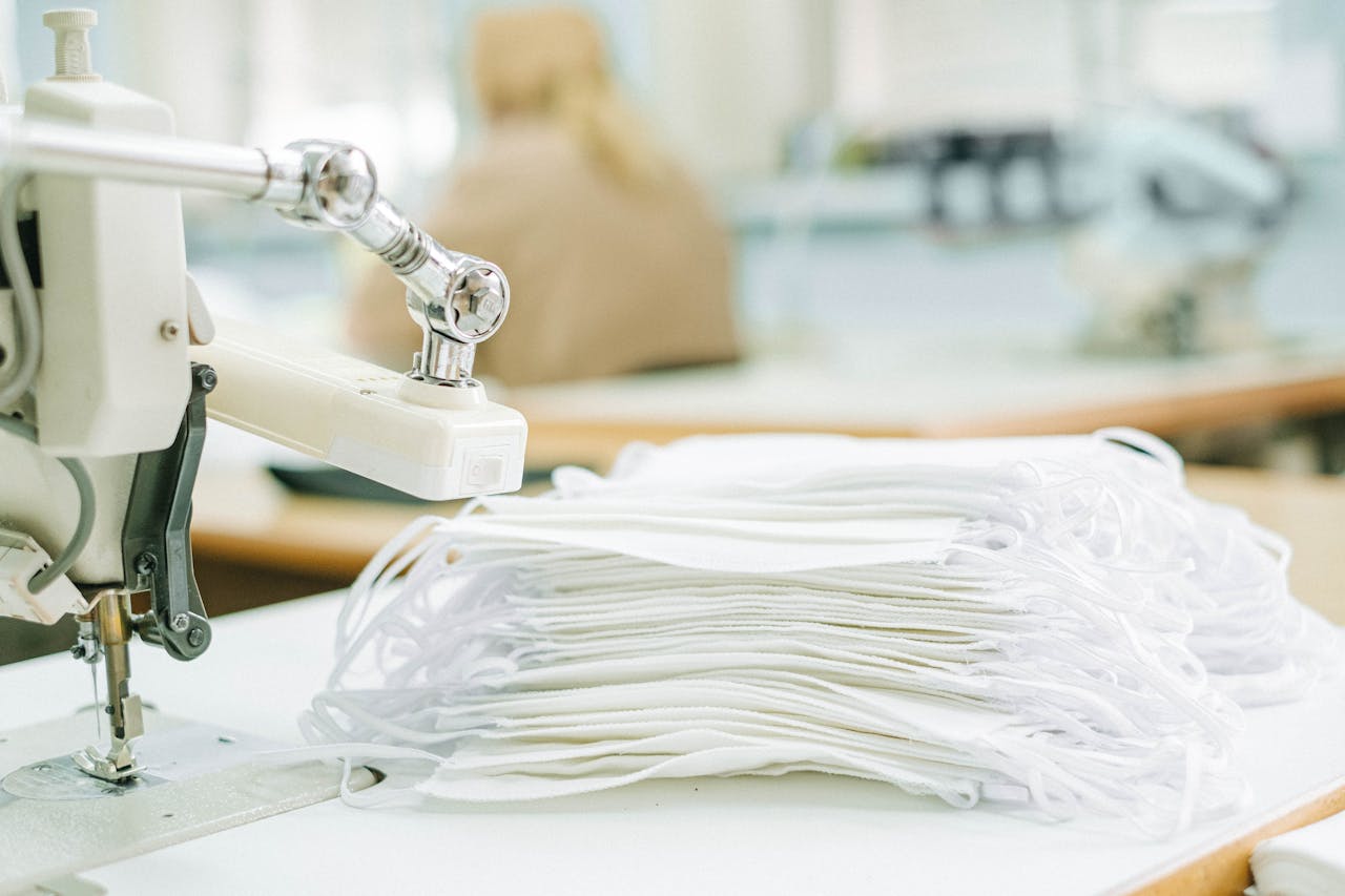 A sewing machine with a stack of white face masks in a textile production setup.